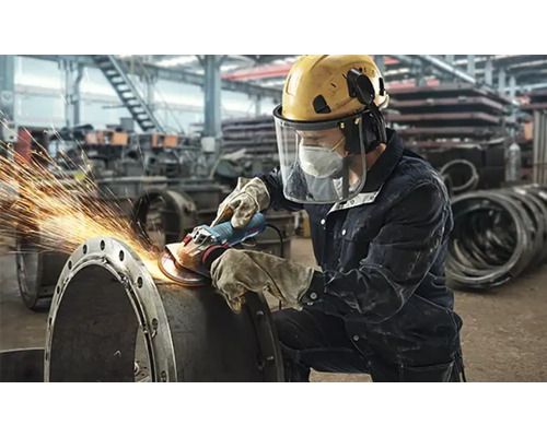 Mann schleift Metallrohr mit Winkelschleifer, Funken fliegen, persönliche Schutzausrüstung