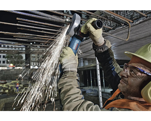 Ein Bauarbeiter verwendet einen Winkelschleifer zum Schneiden von Armierungseisen, wobei Funken fliegen.