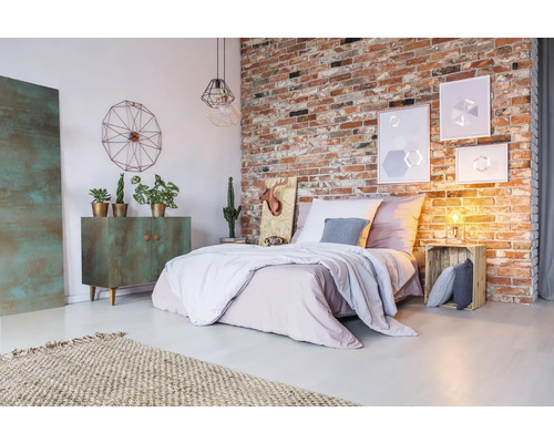 Schlafzimmer mit Ziegelwand, Bett, Kommode, Teppich und dekorativen Elementen