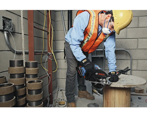 Ein Bauarbeiter mit Schutzkleidung benutzt eine Bosch Kreissäge auf einer Baustelle.