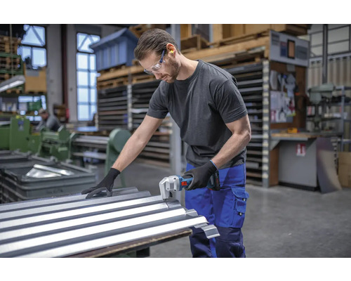 Ein Mann schneidet Wellblech mit einer Blechschere in einer Werkstatt.