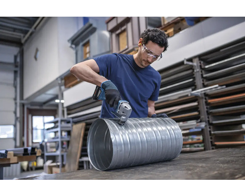 Ein Mann schneidet mit einer Blechschere ein Lüftungsrohr aus Metall.