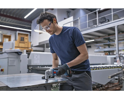 Handwerker mit Sicherheitsausrüstung schneidet Blech mit einer Blechschere in einer Werkstatt.