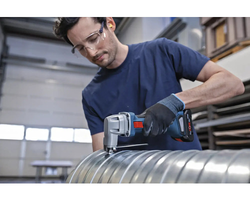 Handwerker schneidet Metallrohr mit einer Akku-Blechschere