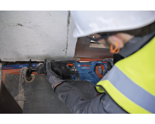 Ein Bauarbeiter mit Schutzhelm und Schutzweste verwendet eine Säbelsäge der Marke Bosch, um ein Rohr zu schneiden.