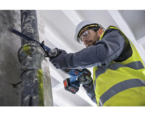 Ein Mann mit Schutzhelm und Schutzbrille sägt mit einer Säbelsäge ein Rohr.