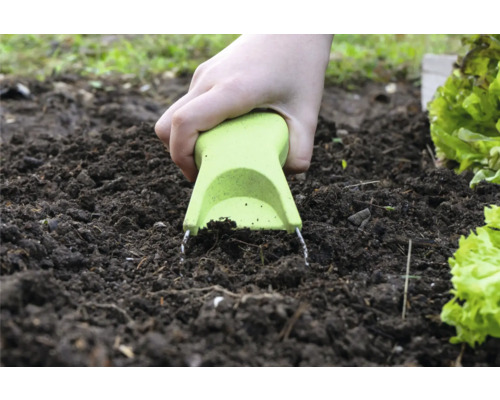 Eine Hand benutzt einen Jäter im Gartenboden.