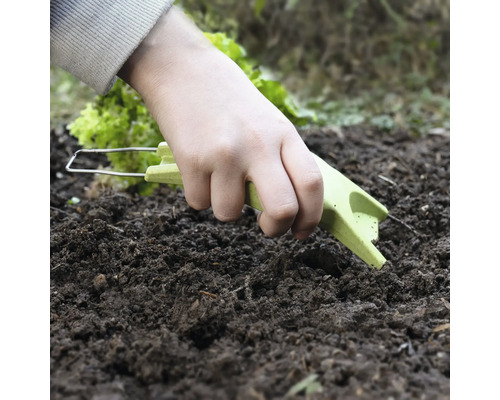 Eine Hand benutzt eine Gartenkralle im Erdreich.