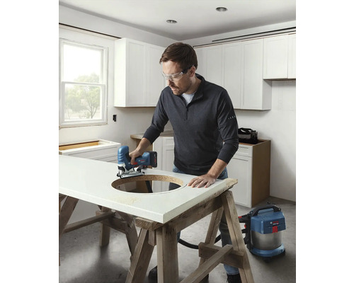 Ein Mann sägt mit einer Stichsäge ein Loch in eine Arbeitsplatte in einer hellen Küche.