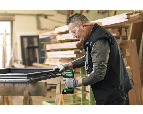 Ein Handwerker montiert mit einem Akku-Bohrschrauber ein Fenster auf einer Werkbank.