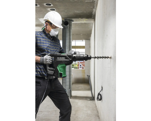 Ein Mann bohrt mit einem Bohrhammer der Marke HiKOKI ein Loch in eine Betonwand.