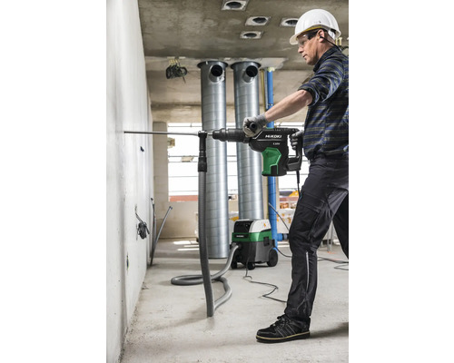 Mann bohrt mit einem Bohrhammer ein Loch in eine Wand, während ein Industriesauger den Staub absaugt.