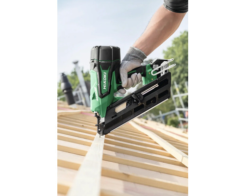 Eine Person befestigt mit einem grünen HiKoki Akku-Nagler ein Holzbrett auf einem Dachstuhl.