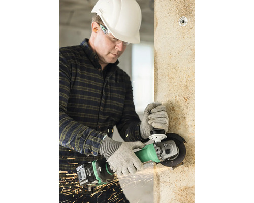 Handwerker mit Schutzhelm und Schutzbrille bearbeitet eine Wand mit einem Winkelschleifer, wobei Funken entstehen.