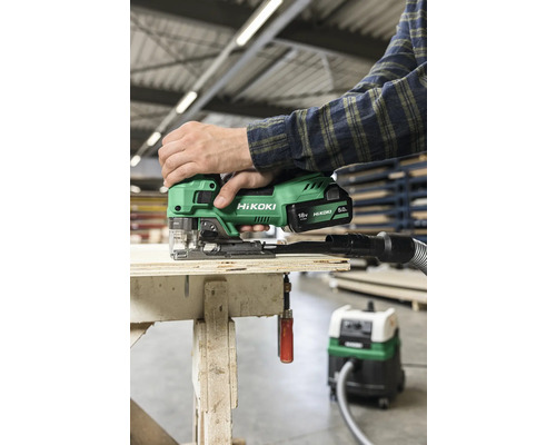 Person benutzt eine grüne Akku-Stichsäge von Hikoki auf einer Holzoberfläche mit einem Staubsauger angeschlossen.