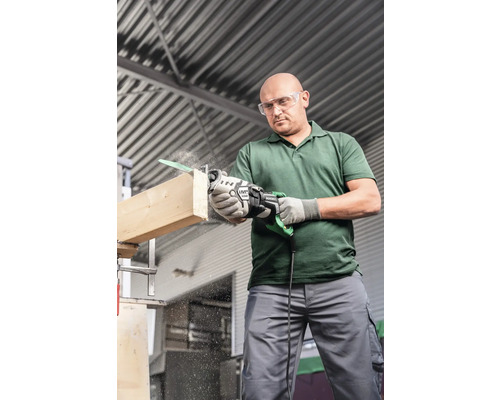 Mann mit Schutzbrille sägt mit einer elektrischen Säbelsäge ein Holzbrett.