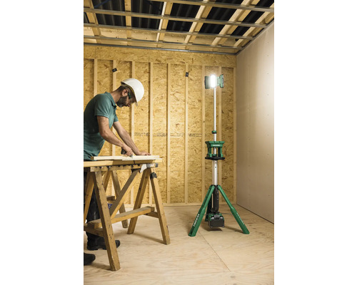 Ein Handwerker bei der Arbeit in einem Rohbau, beleuchtet durch einen Baustrahler.