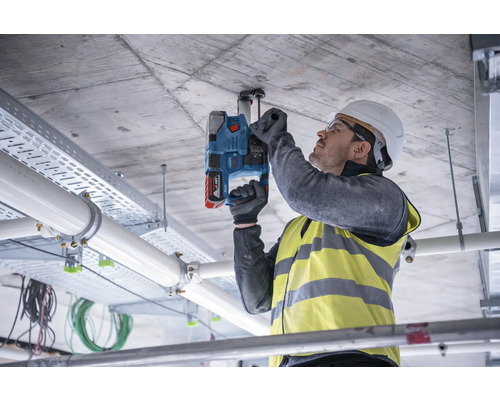 Ein Mann befestigt mit einem Akku-Bohrhammer eine Halterung an einer Betondecke.