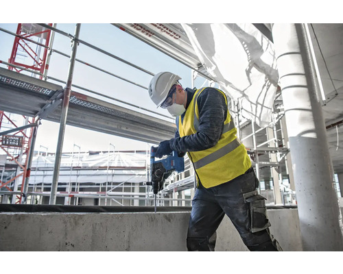Ein Bauarbeiter bohrt mit einer Bohrmaschine in ein Betonstück auf einer Baustelle.
