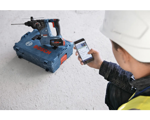 Bohrmaschine auf Werkzeugkoffer, Mann bedient Smartphone