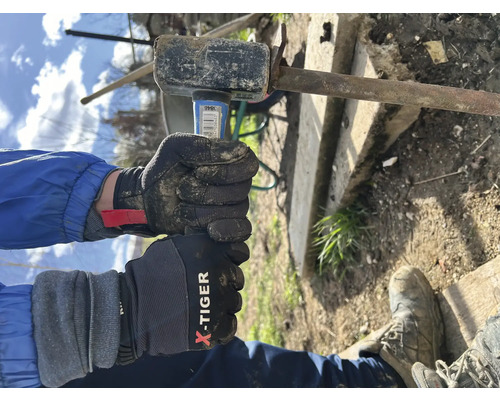 Person mit Handschuhen schlägt mit einem Hammer auf ein Metallstück