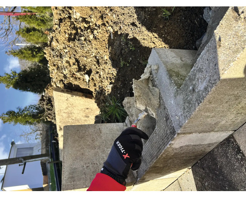 Arbeiter mit Handschuhen bei Reparaturarbeiten an einer Betonmauer im Garten.