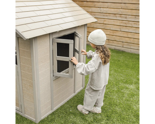 Mädchen öffnet Fenster an einem Spielhaus aus Kunststoff im Garten.