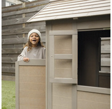 Kind spielt in einem Holzspielhaus im Garten.