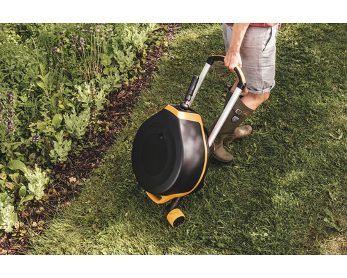 Garten Szene mit einem rotierenden Komposter auf Rädern, der von einer Person auf einem Rasen gehalten wird