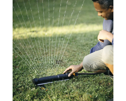 Mann bedient einen Rasensprenger im Garten, der Wasser sprüht.