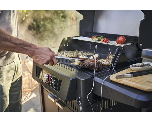 Person grillt Fleisch und Gemüse auf einem Grill mit digitaler Temperaturanzeige.