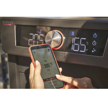 Nahaufnahme eines Grills mit digitalem Display und einer Person, die mit einem Smartphone die Temperatur einstellt.