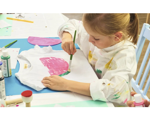 Ein Mädchen bemalt ein T-Shirt mit Farben und einem Pinsel.