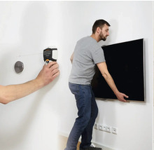 Mann montiert mit einem Nivelliergerät einen Fernseher an einer Wand.