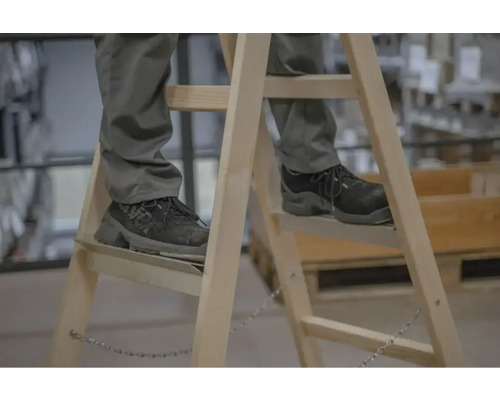 Person auf Holzleiter mit Sicherheitsschuhen
