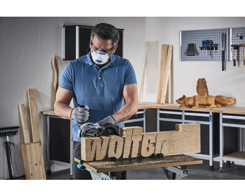 Ein Mann schleift mit einer Schleifmaschine ein Holzstück mit dem Schriftzug Wolter.