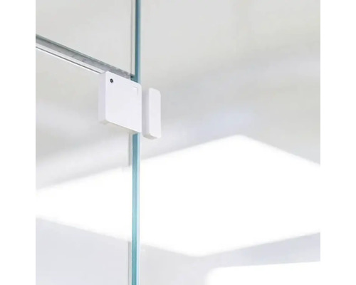 Weißer Fenster- oder Türkontaktsensor an einer Glasscheibe befestigt