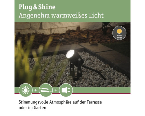 Garten Szene mit einem schwarzen Gartenstrahler, der warmweißes Licht ausstrahlt und durch ein Stecksystem mit Strom versorgt wird.