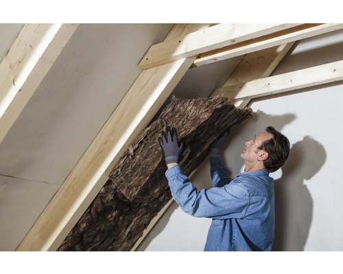 Mann dämmt ein Dach mit Dämmwolle zwischen Holzsparren.