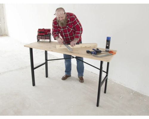 Ein Mann arbeitet an einem Holztisch mit Werkzeugen wie Schraubendrehern, einer Handsäge und einer Sprühdose.