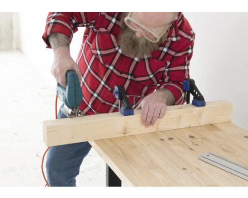 Mann sägt Holzbrett mit Stichsäge auf Holztisch