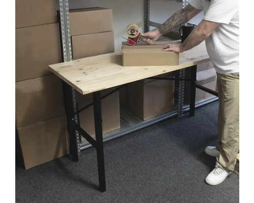 Eine Person verpackt einen Karton mit einem Klebebandabroller auf einem Holztisch in einem Lagerraum.