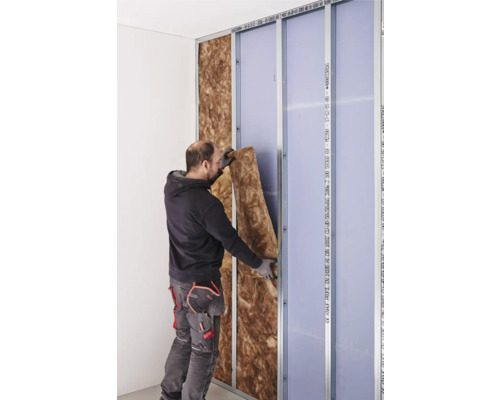 Ein Mann isoliert eine Wand mit Mineralwolle zwischen Metallprofilen und Gipskartonplatten.