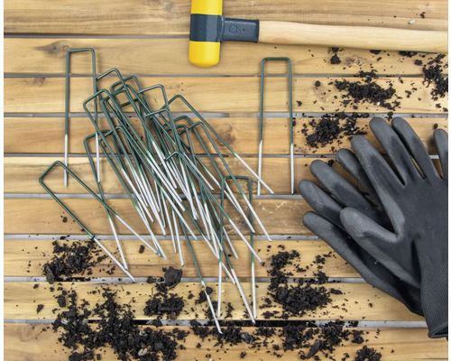 Gartenbild mit Heringen, Gummihammer und Gartenhandschuhen auf Holztisch