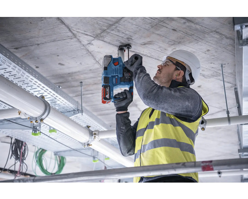 Ein Mann bohrt mit einer Schlagbohrmaschine in eine Betondecke, um eine Befestigung anzubringen.