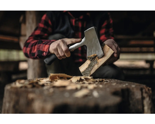 Mann spaltet Holzscheit mit einer Spaltaxt auf einem Hackklotz