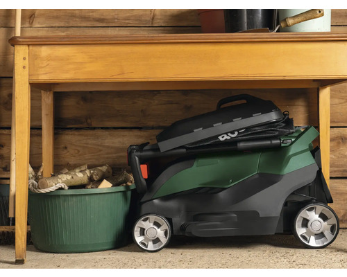 Zusammengeklappter Rasenmäher unter einem Holztisch in einer Garage.