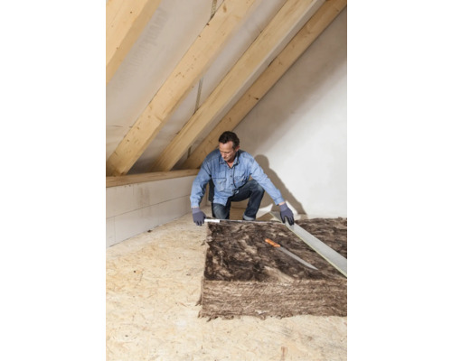 Mann misst Dämmmaterial für den Dachausbau.
