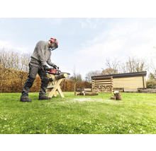 Eine Person sägt mit einer Kettensäge Holz auf einer Holzkonstruktion im Garten.