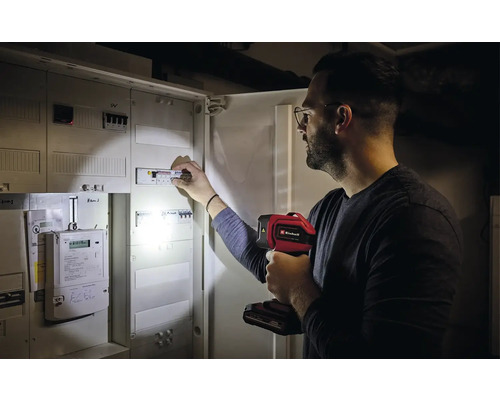 Ein Mann überprüft mit einer Einhell Lampe einen Sicherungskasten.
